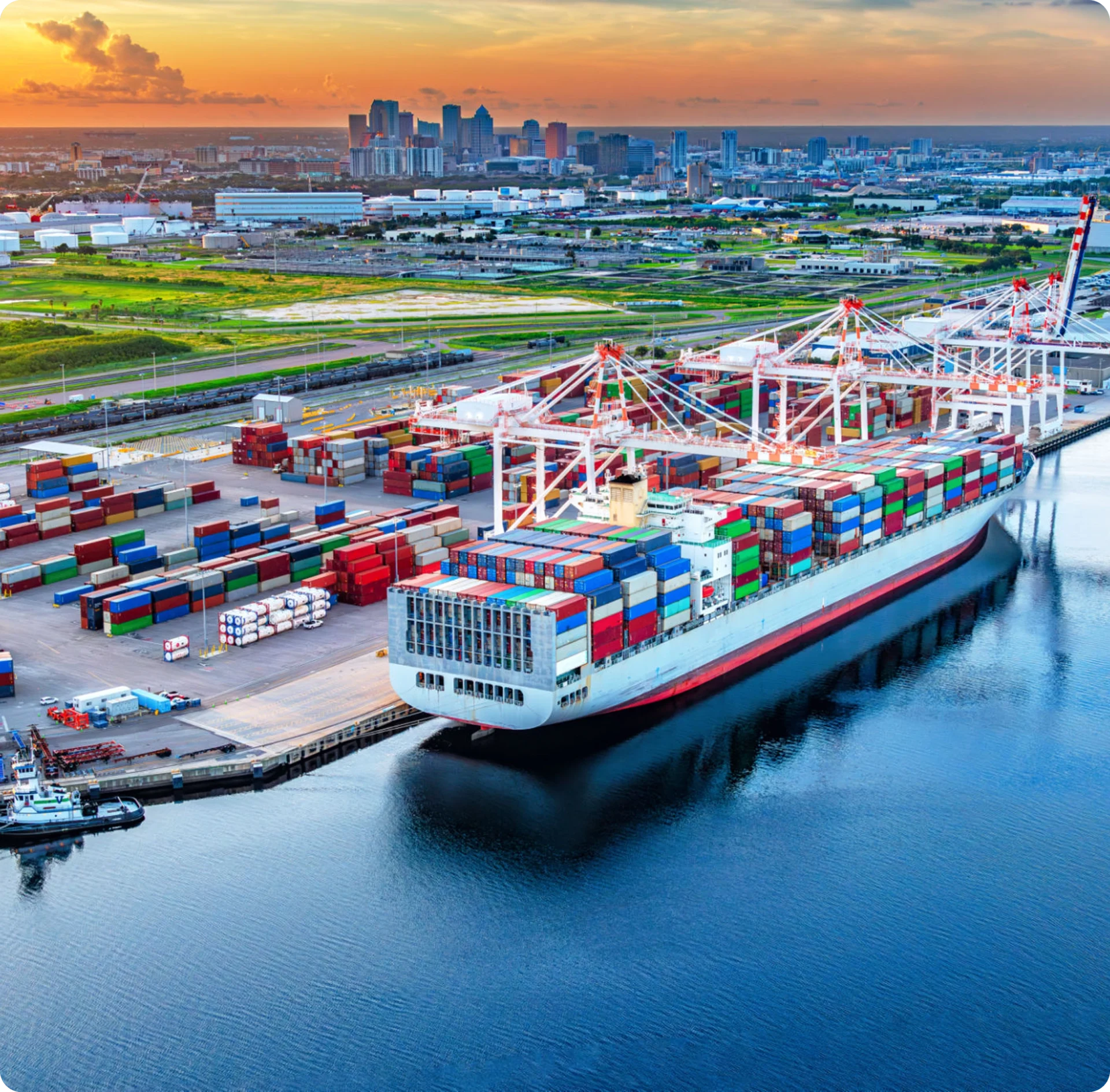 Cargo ship docked at busy port, sunset.